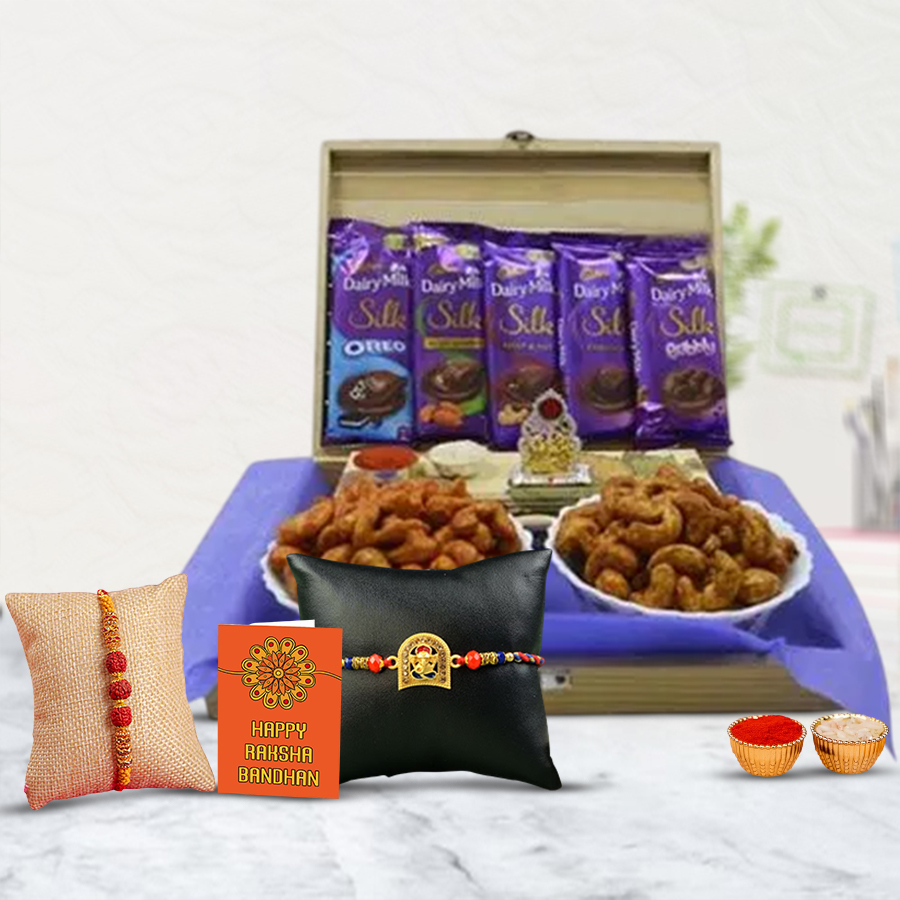 Classy Rakhi set featuring Rudraksha and Ganesh Rakhis, Laxmi Ganesh Mandap, assorted Cadbury Dairy Milk Silk chocolates, cheese and pizza-flavored cashews in a reusable wooden gift box, along with Roli Tilak, chawal, and a personalized Rakhi card.