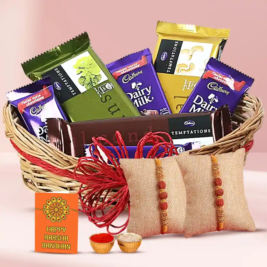 A beautifully arranged cane basket filled with Cadbury Dairy Milk and Temptation chocolates, two Rudraksha Rakhis, and packets of Roli, Tilak, and Chawal, symbolizing the celebration of Raksha Bandhan.