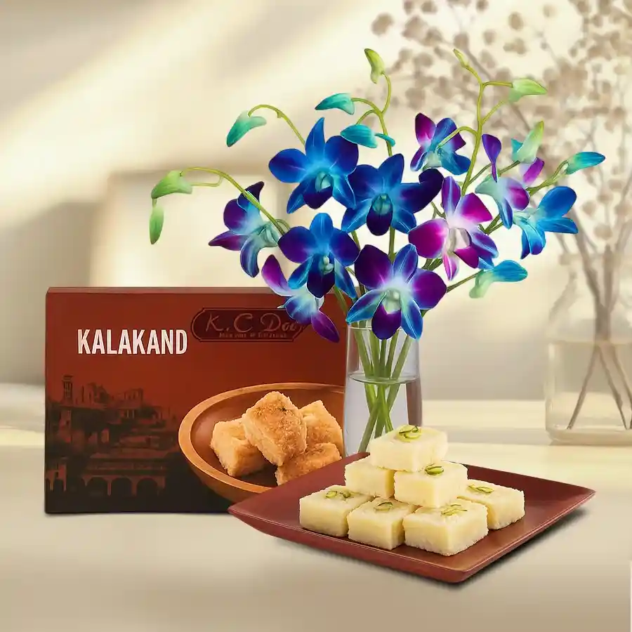 Elegant arrangement of mixed orchids in a glass vase paired with Kalakand sweets.